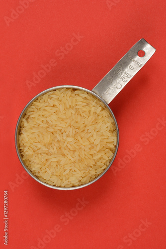A top-down shot of a stainless steel measuring cup filled with rice against a solid red background