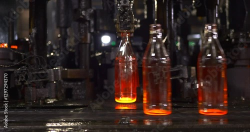 glowing molten glass bottles formed by automated machinery forming into precise bottle shapes, moving through a high-speed manufacturing process at an industrial glass factory ensuring efficiency