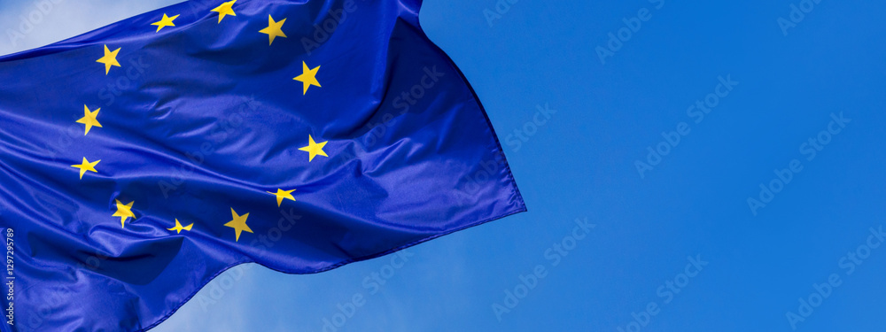 Flag of the European Union waving in the wind on flagpole against the sky with clouds on sunny day, banner, close-up