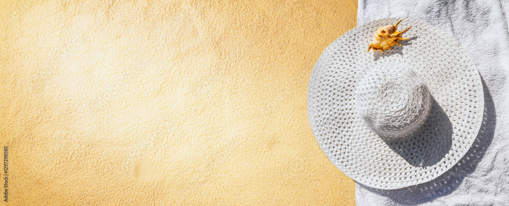 Top view of a beach hat with towel and seashell on the sand under the hot summer sun, horizontal banner. Concept of sandy beach holiday, flat lay, background with copy space for text