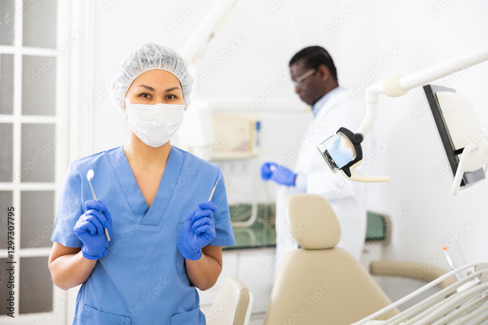 Obraz premium Portrait of a nurse with tools in her hands and wearing a medical mask in a dental office