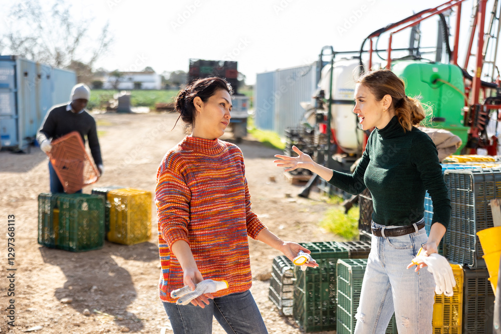 Obraz premium Asian and Caucasian women agriculturists quarreling about work outdoors.