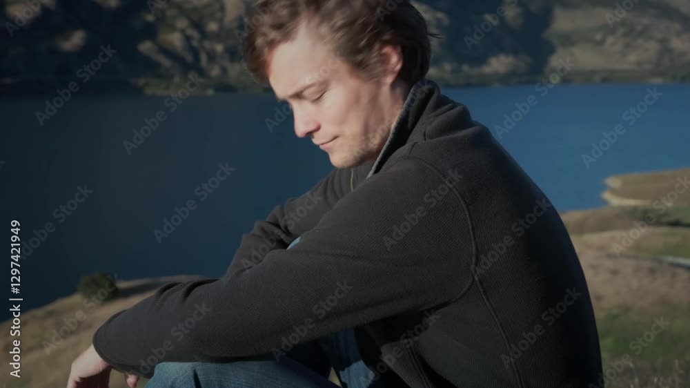 a man relaxing on the side of a lake in the mountains. a man relaxing on the side of a lake in the mountains.
