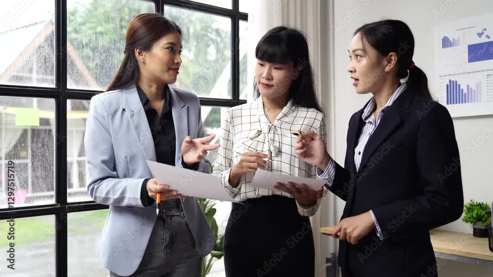 Professional Asian businesswomen collaborating near large office window, analyzing paperwork while exchanging strategic insights and fostering innovative teamwork in corporate environment Professional Asian businesswomen collaborating near large office window, analyzing paperwork while exchanging strategic insights and fostering innovative teamwork in corporate environment