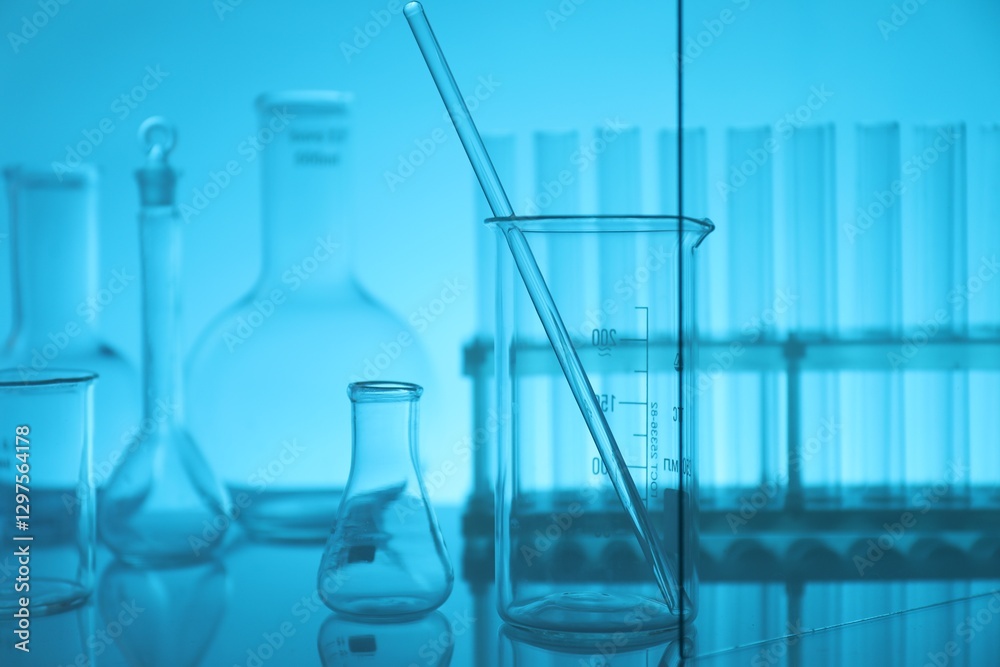 Laboratory glassware on mirror surface against light blue background Laboratory glassware on mirror surface against light blue background