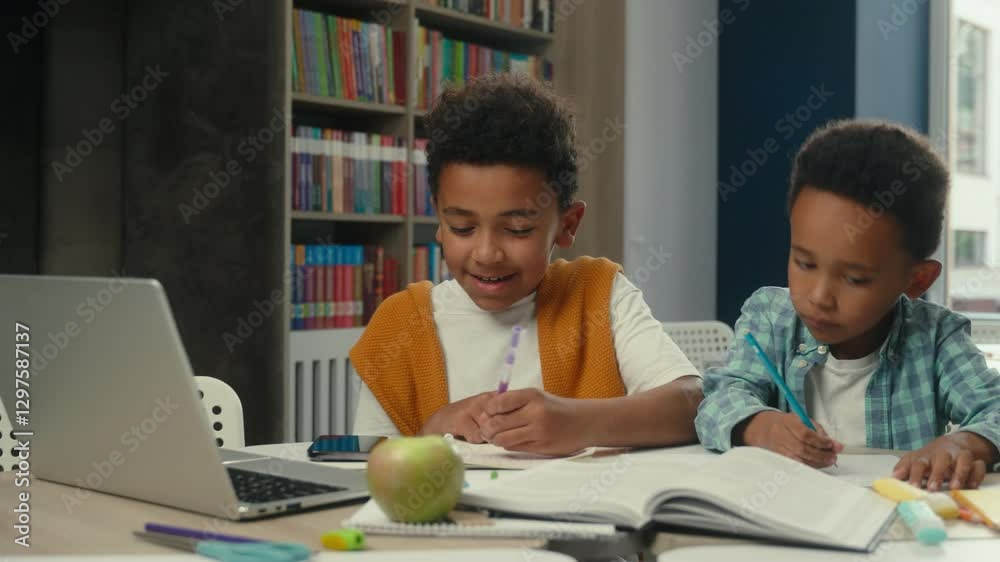 African American little boys siblings brothers children kids students schoolboys pupils studying writing together at desk primary school online education laptop internet teacher video call e-learning