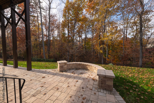 A serene backyard with a curved stone wall and patio pavers, surrounded by bare trees, autumn foliage, and scattered leaves.
