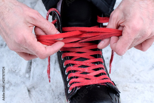 Man laces up hockey skates on an ice skating rink. Ice skating outdoors. Winter sport. Red laces.