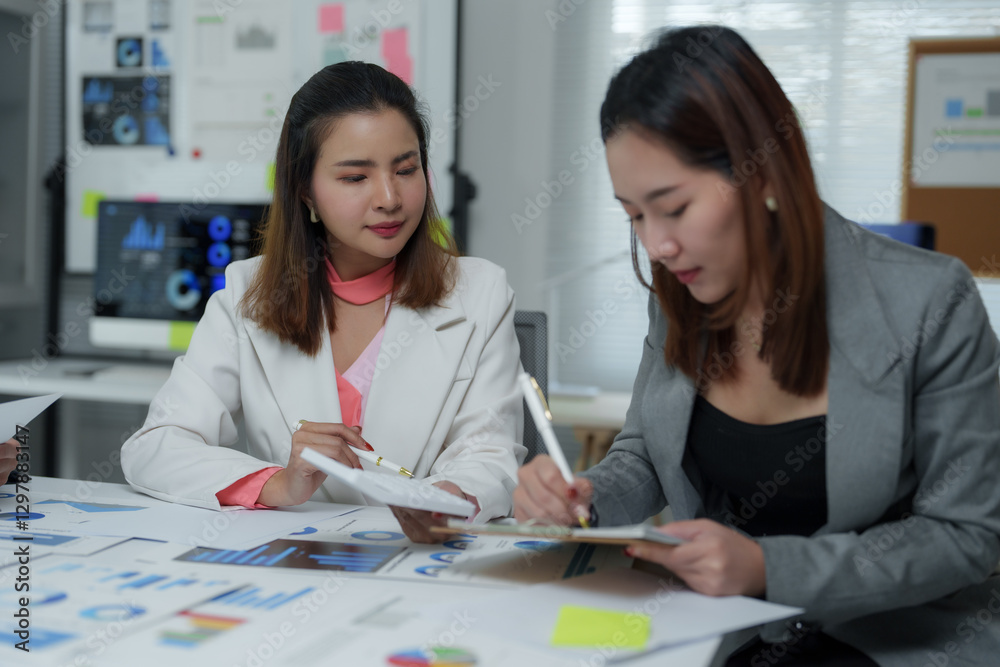 Businesswomen working together analyzing financial charts in office meeting Businesswomen working together analyzing financial charts in office meeting