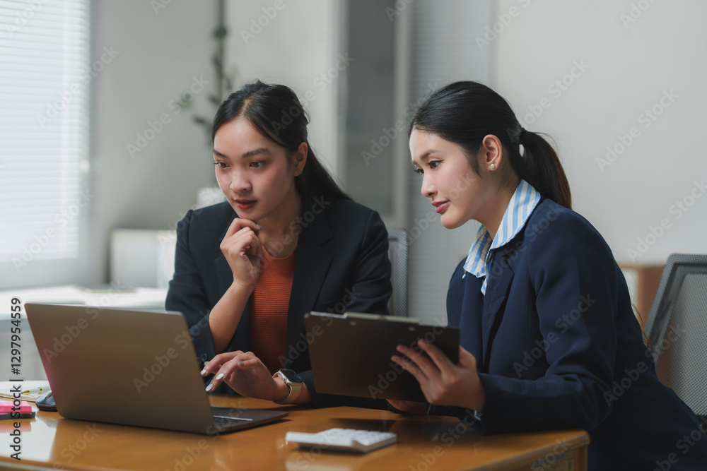 Businesswomen working together using laptop and documents in office Businesswomen working together using laptop and documents in office