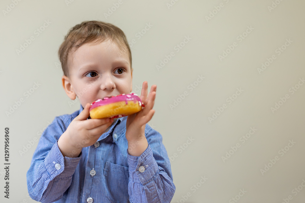 Happy young boy in blue shirt holding pink frosted donut, enjoying a sweet treat. Space for text.