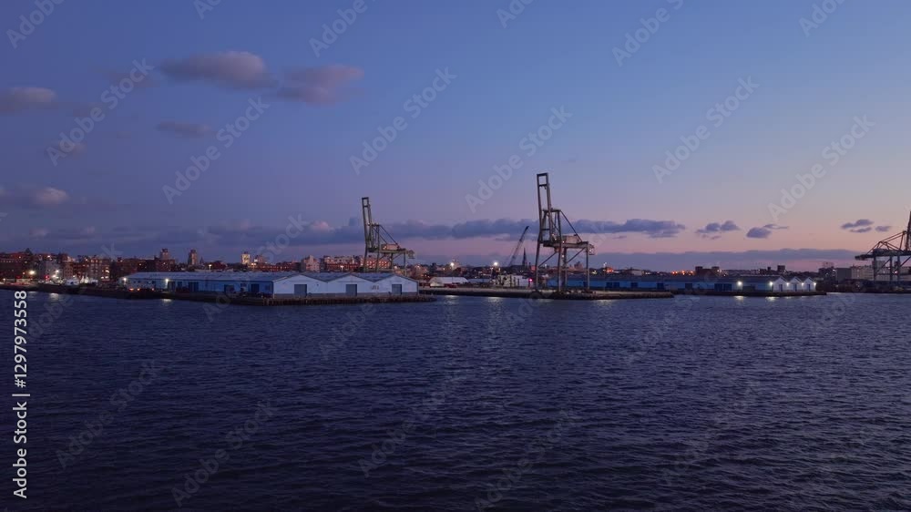 Golden sunset illuminating industrial New York harbor, silhouetting maritime cranes and waterfront warehouses against iconic city skyline Golden sunset illuminating industrial New York harbor, silhouetting maritime cranes and waterfront warehouses against iconic city skyline