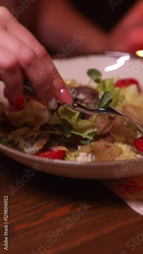 close-up of a salad plate, a woman's hand with a fork. The fork in the salad is stirring