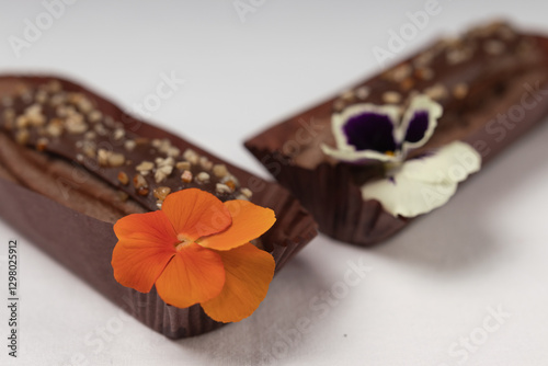 Two chocolate ?clairs in focus, one with an orange edible flower and another with a white and purple flower, creating a visually appealing contrast.