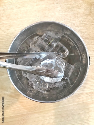 Ice and ice tongs in a stainless steel bucket. 