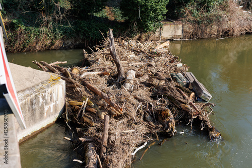 Mass of tangled dead drift wood  logs dried foliage waste garbage accumulate concrete  blocking bridge pillar protection barrier on river at springtime flood. Jam wooden logs water flow blockage