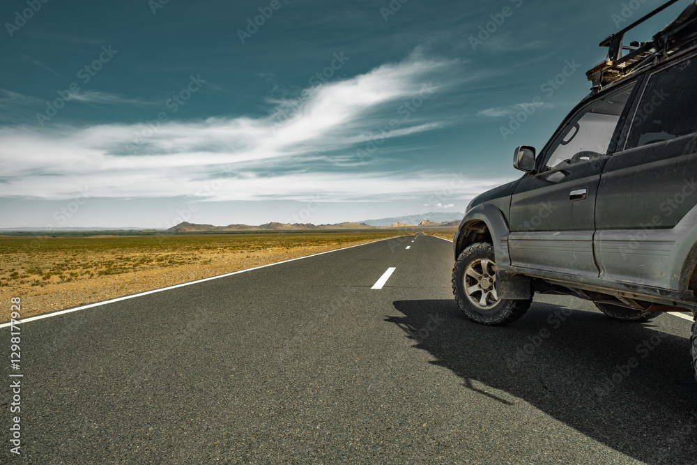 An off-road vehicle for traveling on mud off-road tires, stands on the road with a view of the steppe and the sky. The travel car is parked on the road. An off-road vehicle for traveling on mud off-road tires, stands on the road with a view of the steppe and the sky. The travel car is parked on the road.
