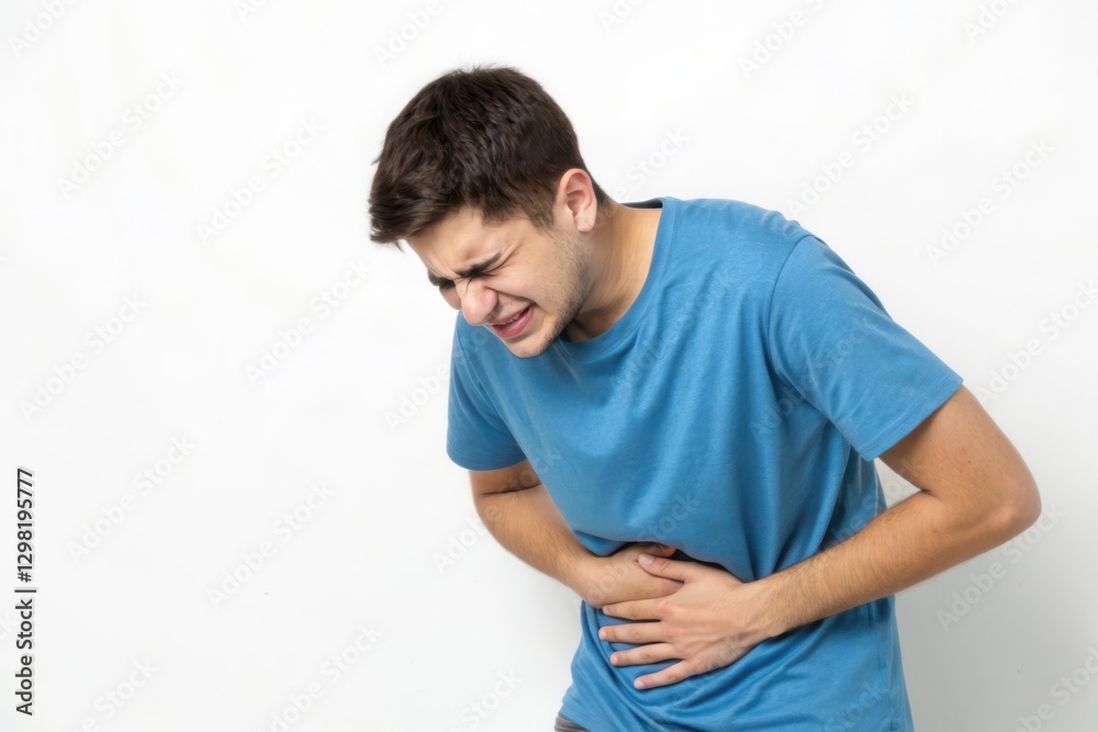 Young Man in Blue Shirt Expressing Discomfort While Holding His Stomach Against a Plain White Background Young Man in Blue Shirt Expressing Discomfort While Holding His Stomach Against a Plain White Background
