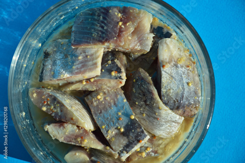 a piece of herring in a glass dish. healthy, salty, fatty fish in oil with spices. background for the design. the blue color.