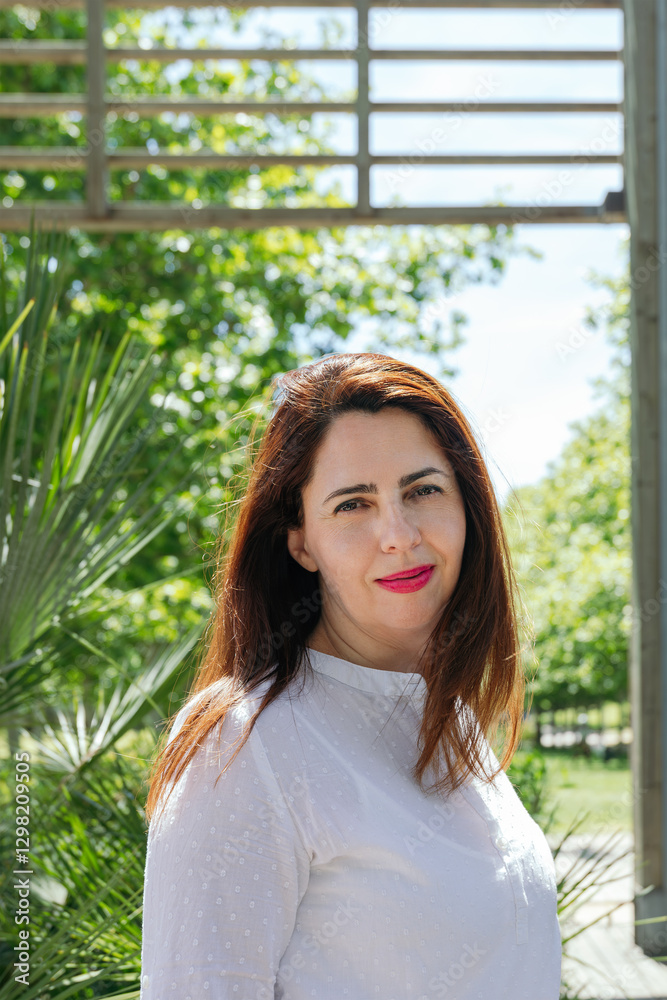 Portrait of smiling mature woman in white shirt, enjoying the natural environment with trees and a wooden structure. Copy space. Concept of joy, tranquility and outdoor life Portrait of smiling mature woman in white shirt, enjoying the natural environment with trees and a wooden structure. Copy space. Concept of joy, tranquility and outdoor life