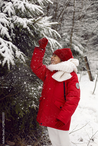 Obraz na płótnie A cheerful seven-year-old boy in a red jacket walks outside in the winter in the forest and plays with snow during the day in clear weather w salonie