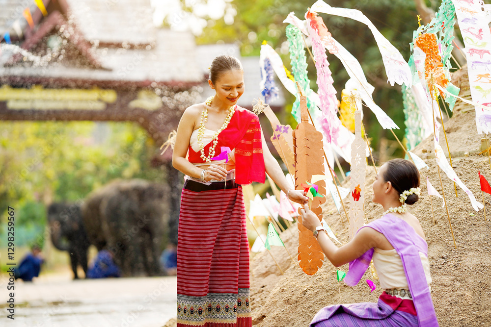 Obraz premium Beautiful Thai women in the Thai traditional dress help stick the triangular flag on the sand pile in temple in Songkran festival.