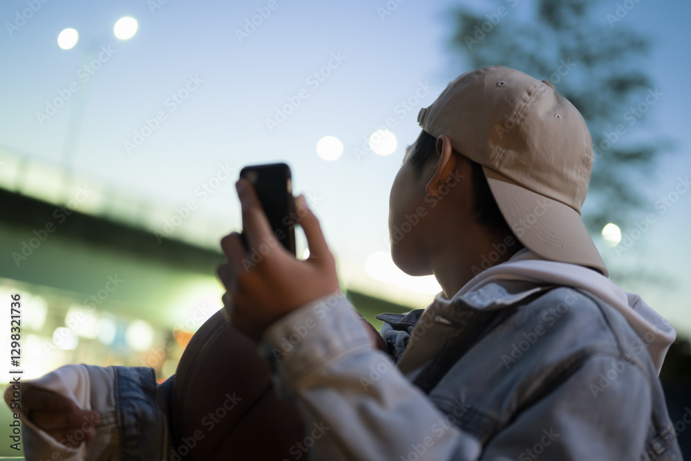 Obraz premium 夕方にバスケットボールとスマホを持って写真を撮る、音楽を聴く、sns投稿する男の子 顔無しのイメージ