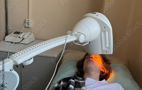 A teenager receiving infrared heat therapy to treat an eye condition. The devices orange light gently warms the eyelid, aiding recovery.