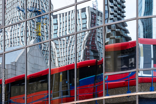 Reflection of a London double-decker bus on a glass facade with urban architecture in the background.
