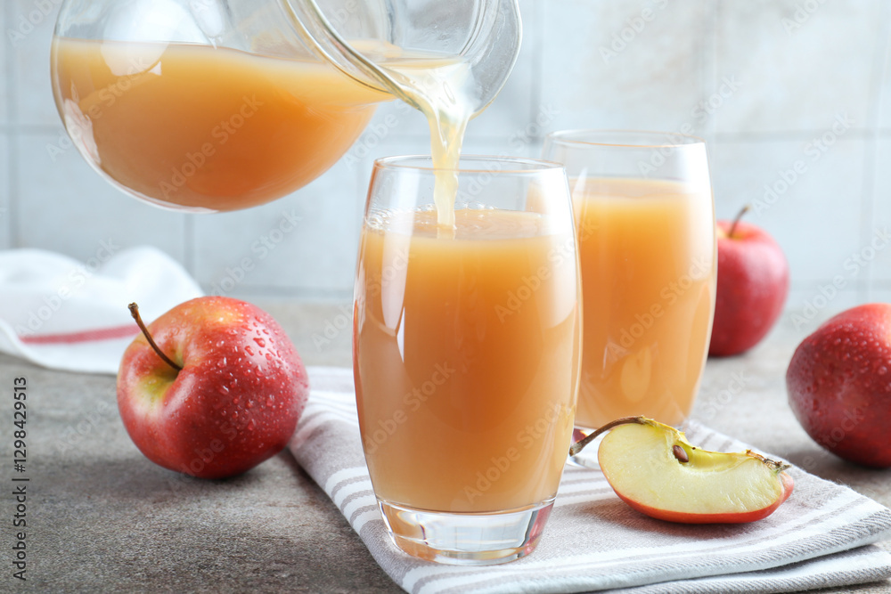 Pouring refreshing apple juice from jug into glass at grey textured table, closeup Pouring refreshing apple juice from jug into glass at grey textured table, closeup
