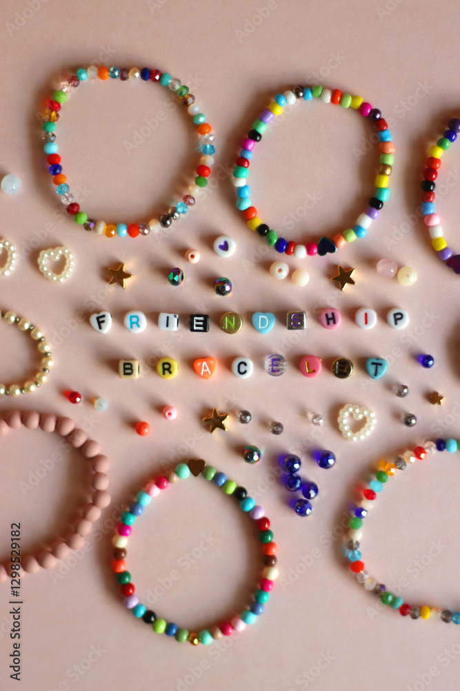 Friendship bracelet spelled with letter beads. Colorful handmade bracelets and various beads. Flat lay, pink background.