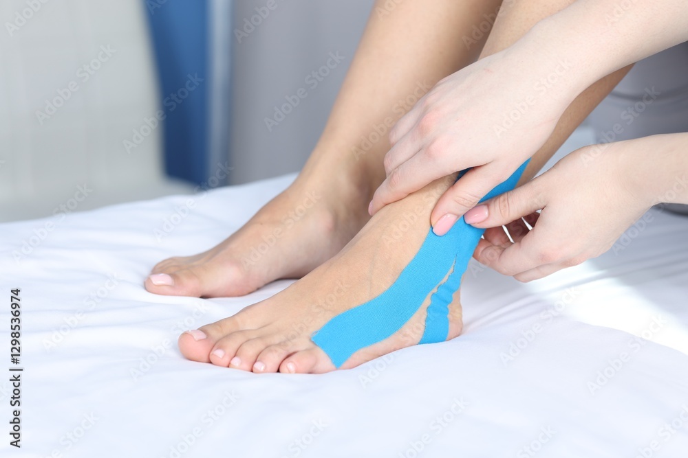 Fototapeta premium Doctor applying kinesio tapes to patient's foot in hospital, closeup