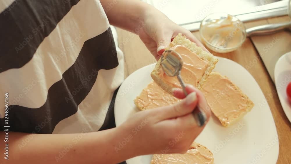 Professional female chef spreading creamy sauce on bread slices while preparing morning meal in sunlit home kitchen Professional female chef spreading creamy sauce on bread slices while preparing morning meal in sunlit home kitchen