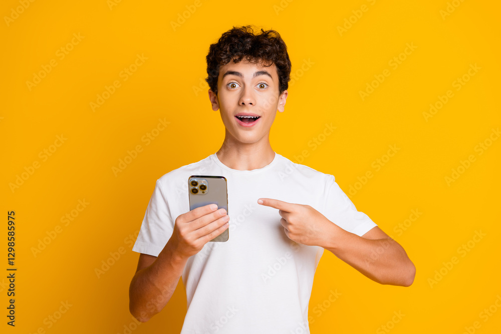 Excited Young Boy Pointing at Smartphone Against Vibrant Yellow Background for Shopping or Lifestyle Concept Excited Young Boy Pointing at Smartphone Against Vibrant Yellow Background for Shopping or Lifestyle Concept