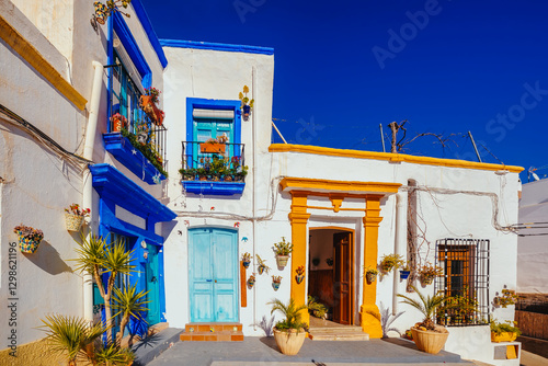 whitewashed facades with coloured windows and doors in a village street decorated with pots and plants. Nijar. Almeria