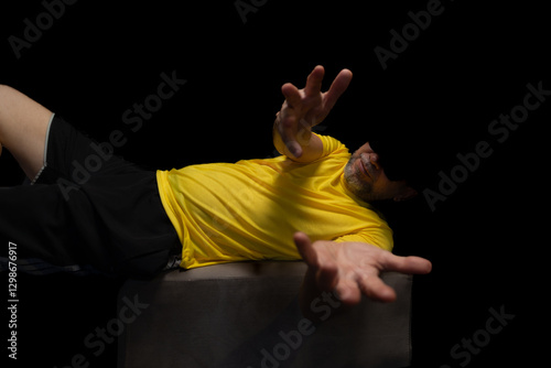 Mature man, 50s, quite uninhibited, with a beard and sunglasses, wearing a hat and yellow shirt posing calmly for a photo sitting on a beanbag.