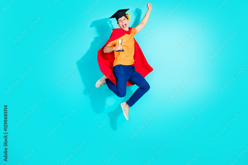 Young enthusiastic graduate with red cape and trophy in hand leaping joyfully on bright turquoise background Young enthusiastic graduate with red cape and trophy in hand leaping joyfully on bright turquoise background