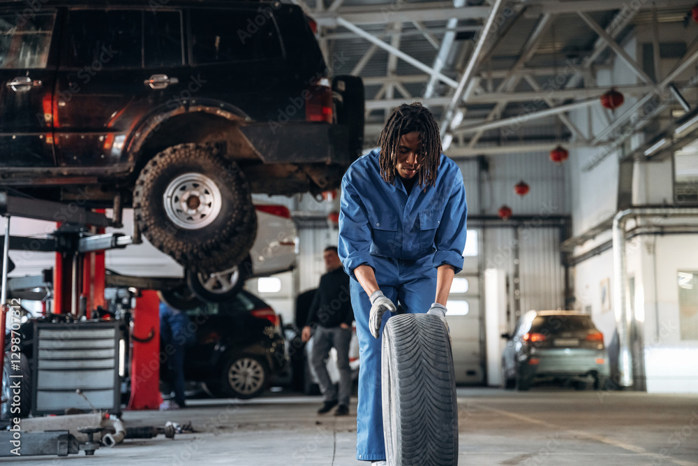 Naklejka premium Brand new tire. Male mechanic is with car in garage