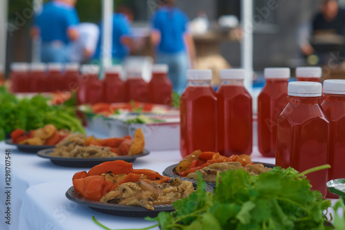Vegetables and drinks on the table outdoors. Preparation for a large corporate lunch. Waiters in blue T-shirts in the blur in the background.