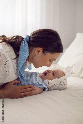 Obraz na płótnie A beautiful brunette woman in a white dress with a baby in a cap lies on the bed at home light from the window. w salonie