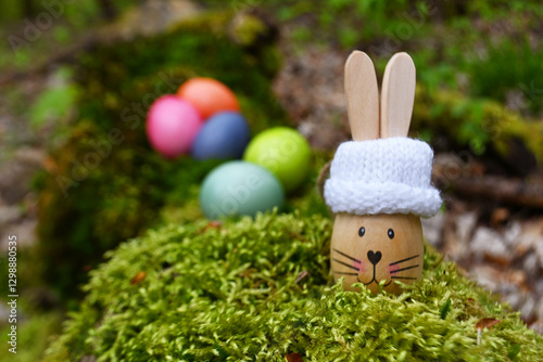Holz-Osterhase mit Mütze und gefärbte Eier auf Moos  im Wald