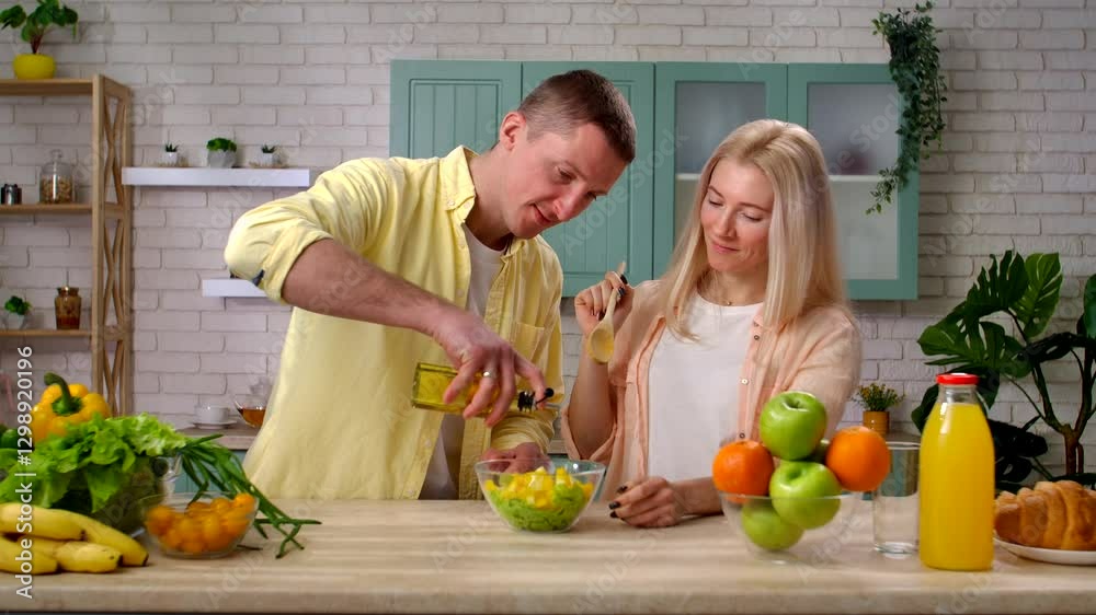 Couple of man and woman in the morning at home in the kitchen at table preparing breakfast, couple making fresh salad bowl, adding oil and mixing. Slow motion. Couple of man and woman in the morning at home in the kitchen at table preparing breakfast, couple making fresh salad bowl, adding oil and mixing. Slow motion.