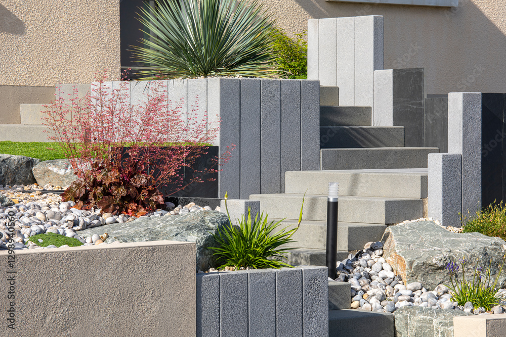 Fototapeta premium Beau jardin paysagé fleuri et ses plantes et palmiers au pied d'une habitation au printemps.