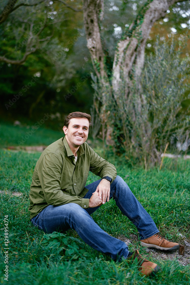 Smiling young man sitting on green grass in the park Smiling young man sitting on green grass in the park