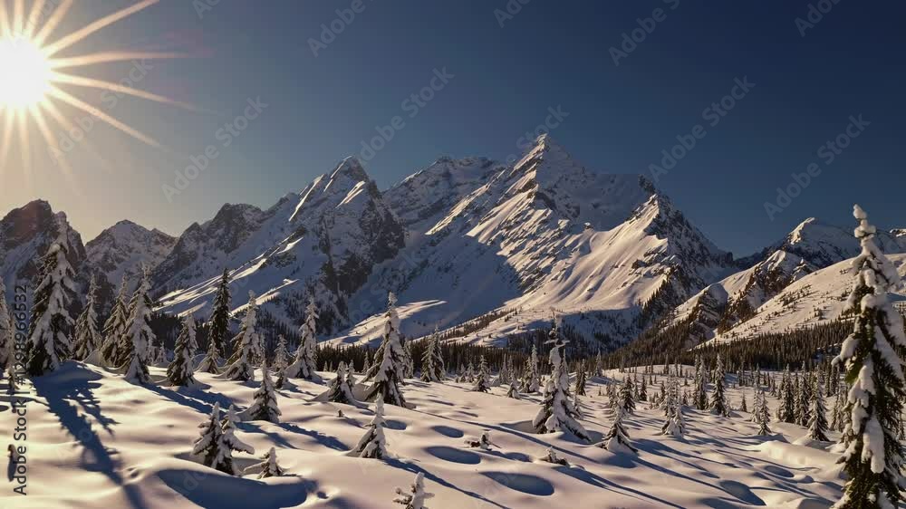 Aerial video captures snow-covered mountains and trees under a bright sun, showcasing a breathtaking winter landscape from a high angle.