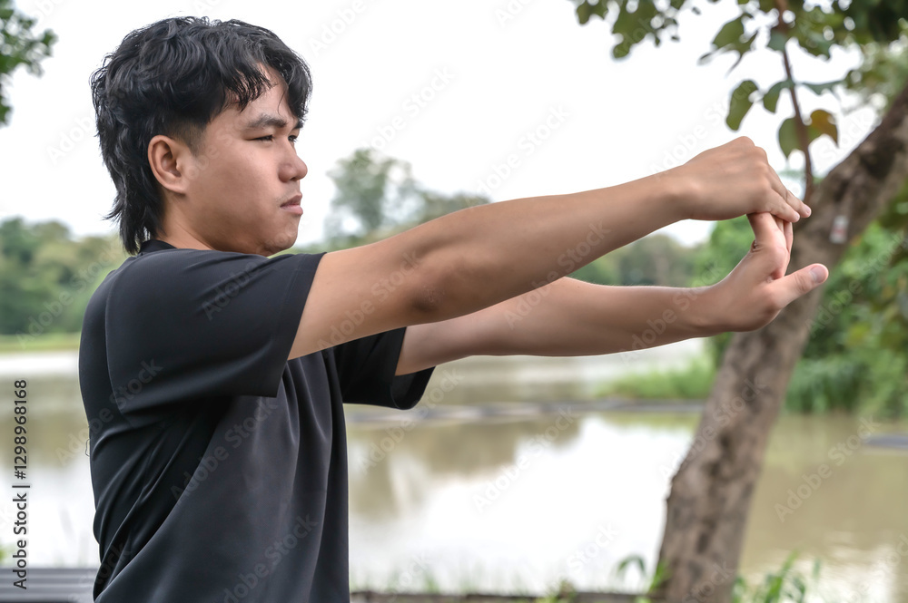 Young Asian male sportsman warm up before doing exercise in green nature park