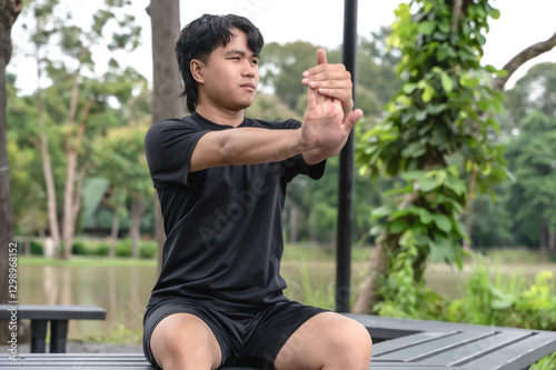 Young Asian male sportsman warm up before doing exercise in green nature park