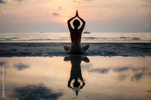 Obraz na płótnie The silhouette of a yoga woman practicing on the beach with her reflection visible in the water. w salonie