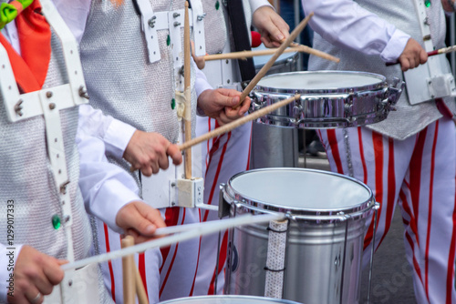 Members of a comparsa play the batucada while advancing in the Tenerife carnival parade, dressed in a white costume with red stripes.