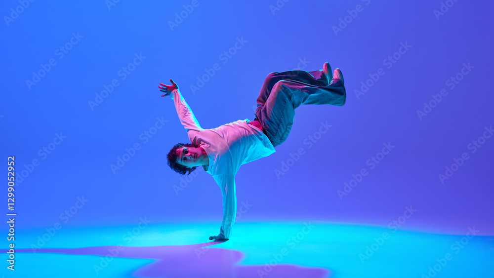 Fototapeta premium Young man, breakdancer blending flexibility, power, and rhythm, performing against gradient blue purple background in neon light. Concept of dance, street style, creativity, youth culture, energy